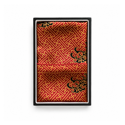 A folded red and gold patterned silk scarf with black dragonmotifs, presented inside a black gift box on a white background.