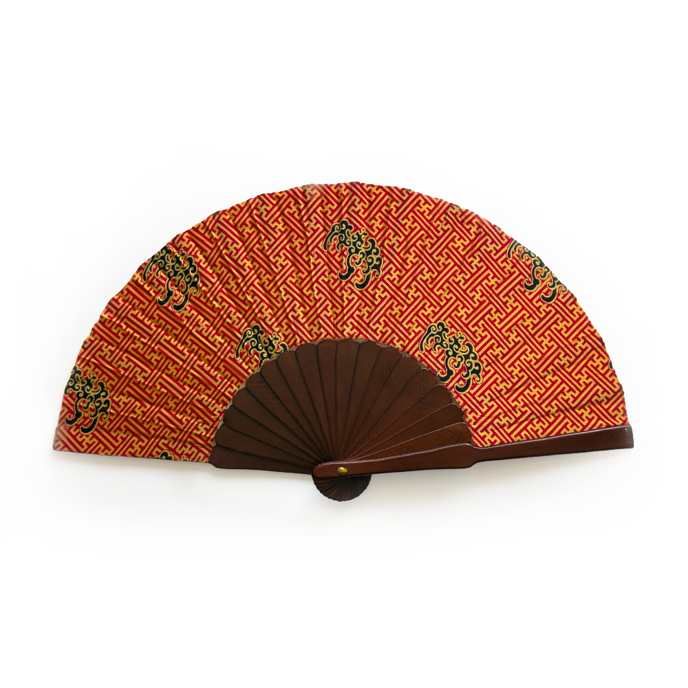 A folding hand fan with a dark brown wooden frame and a red-orange patterned fabric canopy featuring a repeating gold geometric design and black dragon motifs, shown open against a plain white background.