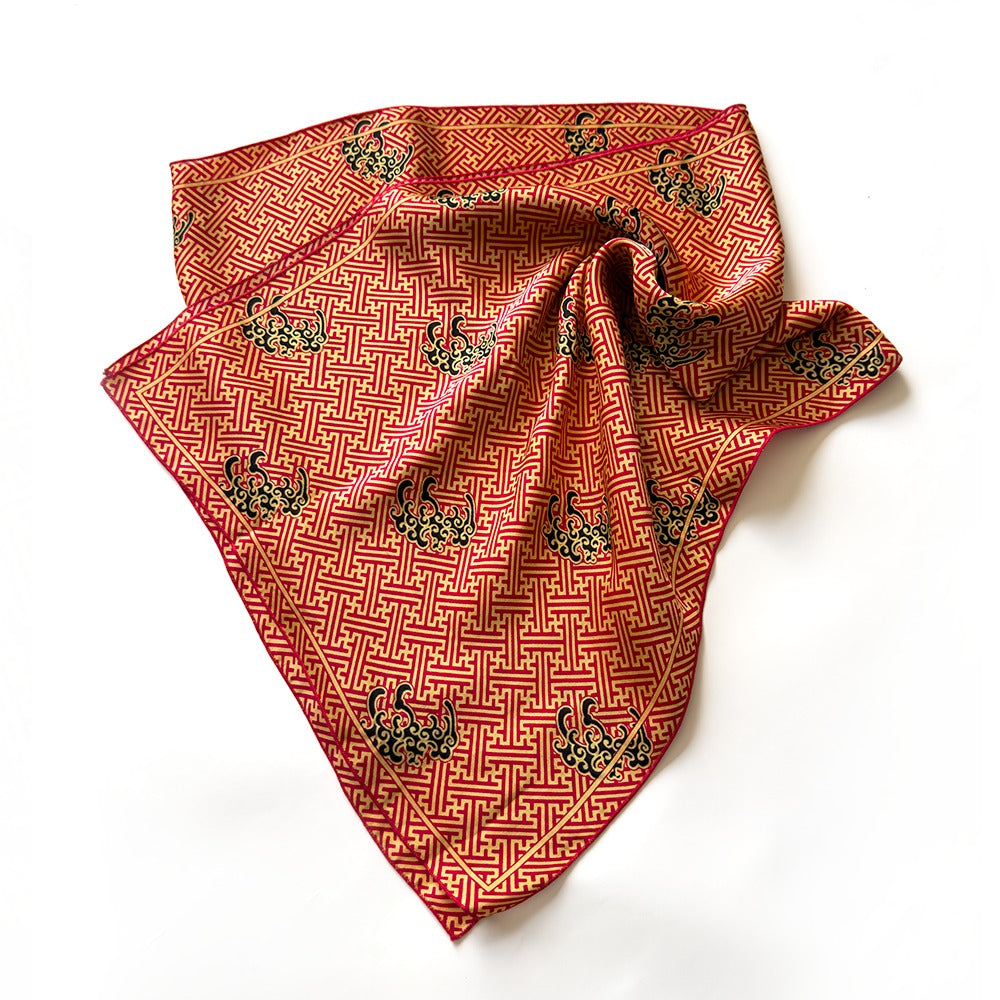 A silk scarf with a red and gold geometric pattern and embroidered swans, laid flat on a white background.